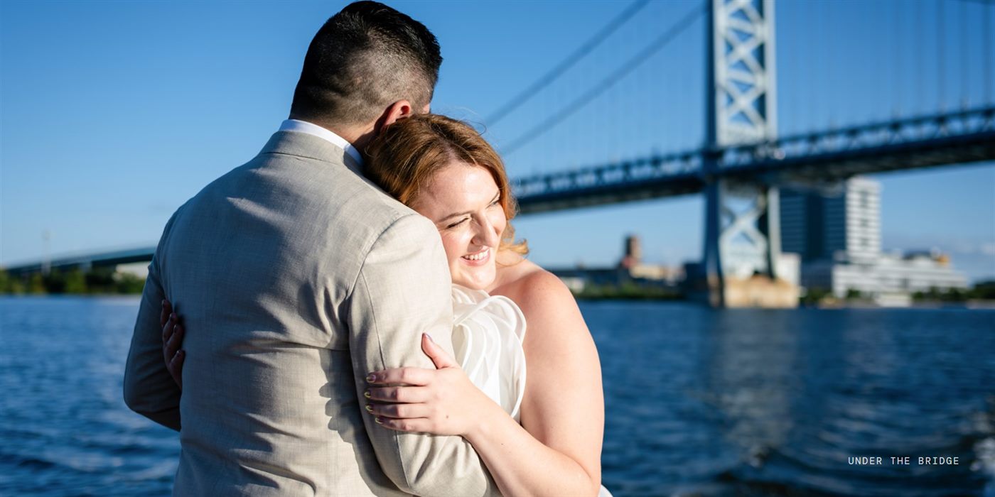 Album spread: one panoramic photo of the couple hugging under the Ben Franklin Bridge